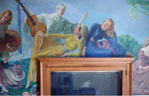 Three women are shown in this part of the mural. The one in front to the left is dressed in yellow and sitting on top of the ticket box, leaning her back against the woman to her right. The woman to the right is dressed in blue and is leaning forward with her head turned to the left. Behind them stands a woman in an all white costume holding out an acoustic guitar.