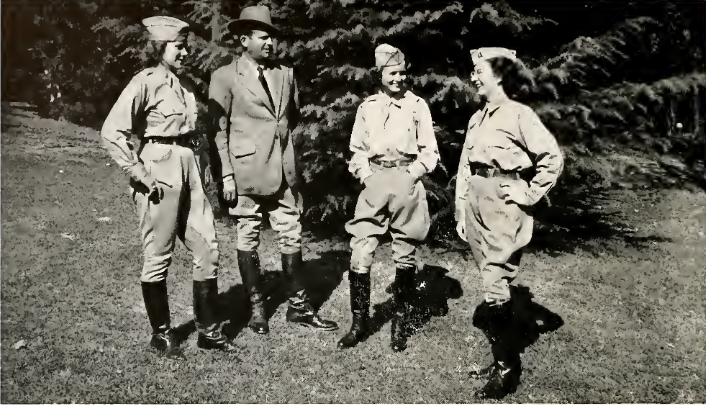 A black and white photo of Calvary Troop members. They are three woman with a man between the first and the second. The women are in uniform and the man wears a suit with a hat.